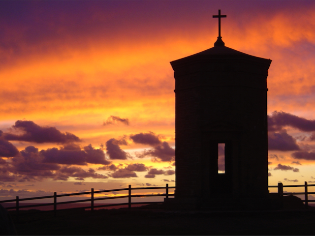 A pepper pot shaped building silhouetted against a fiery orange and purple sunset.