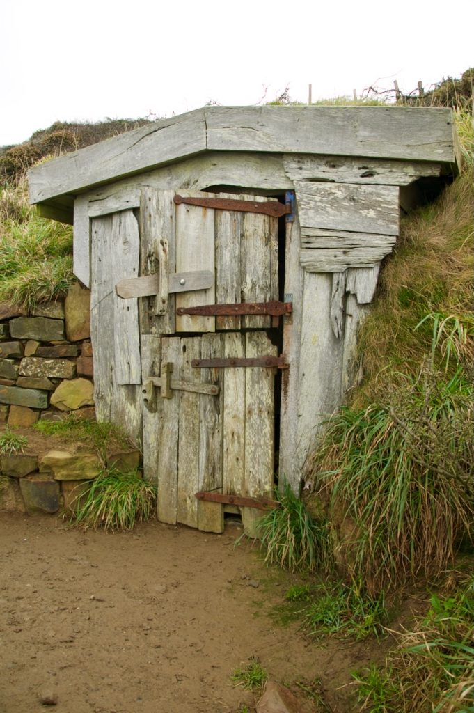 A small hut made from driftwood with a stable door built into the cliff top.