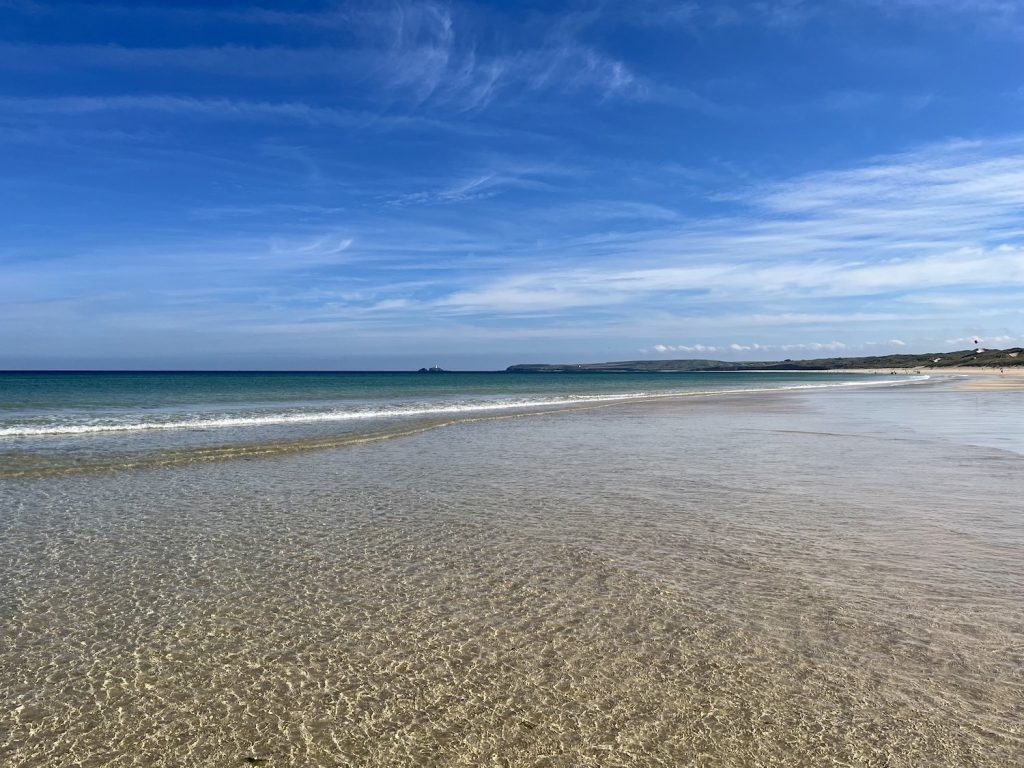 A sandy beach with a gentle wave and blue skies with light cloud.