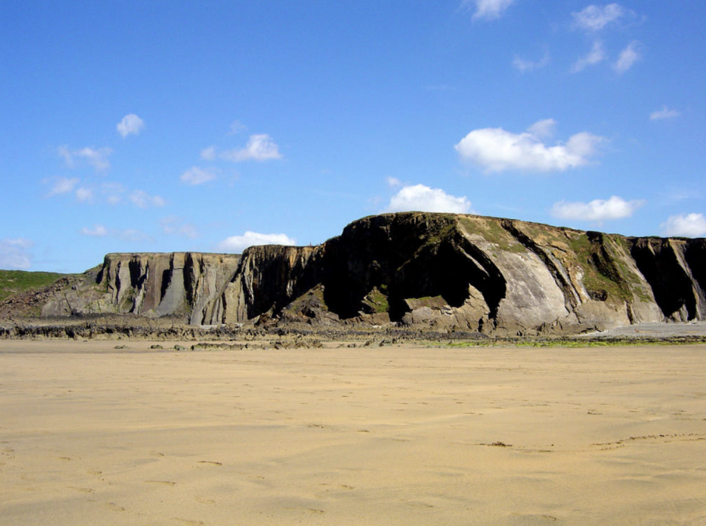 A photograph of a beach with geologically interesting vertical sedimentary rock against a blue sky.