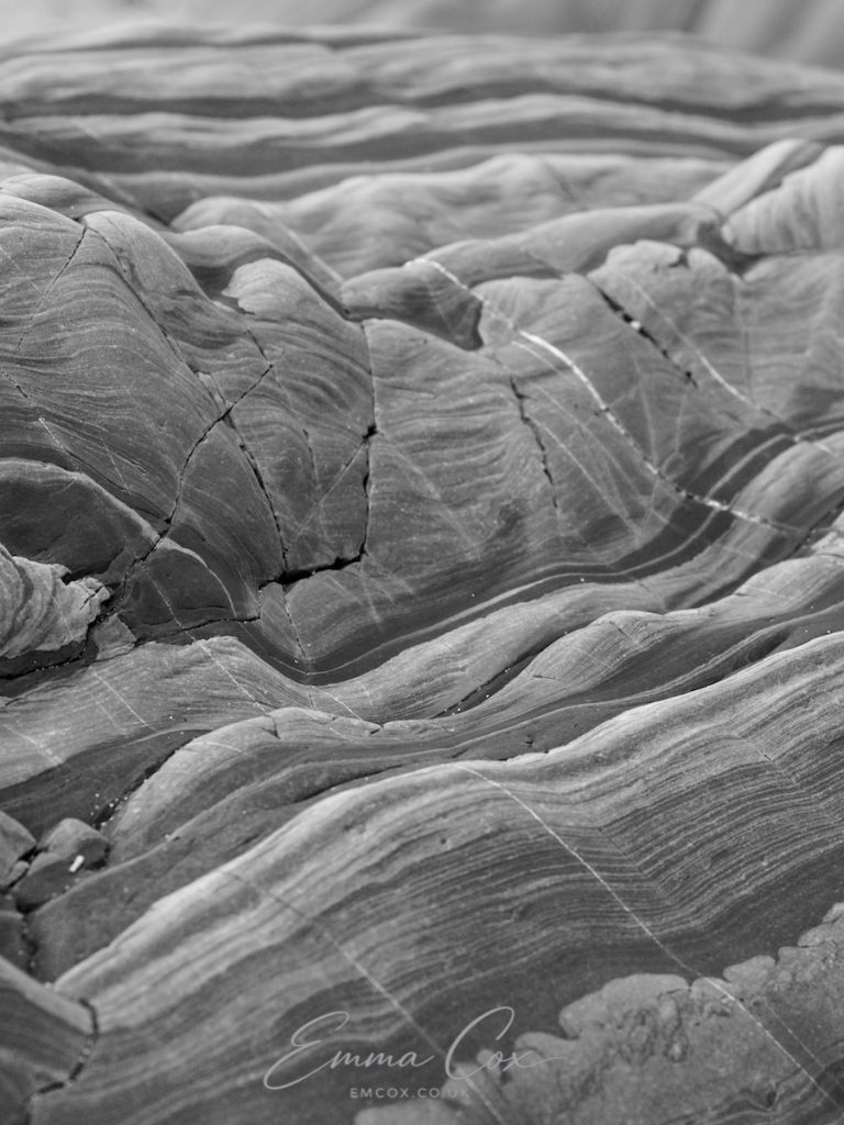 Black and white photograph. Close up of Cornish geology depicting abstract patterns weaving like waves in the rock.