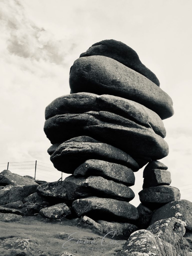 A black and white photograph showing the Cornish geological feature named the Cheesewring. It is a stack of granite stones which look like they might easily topple.