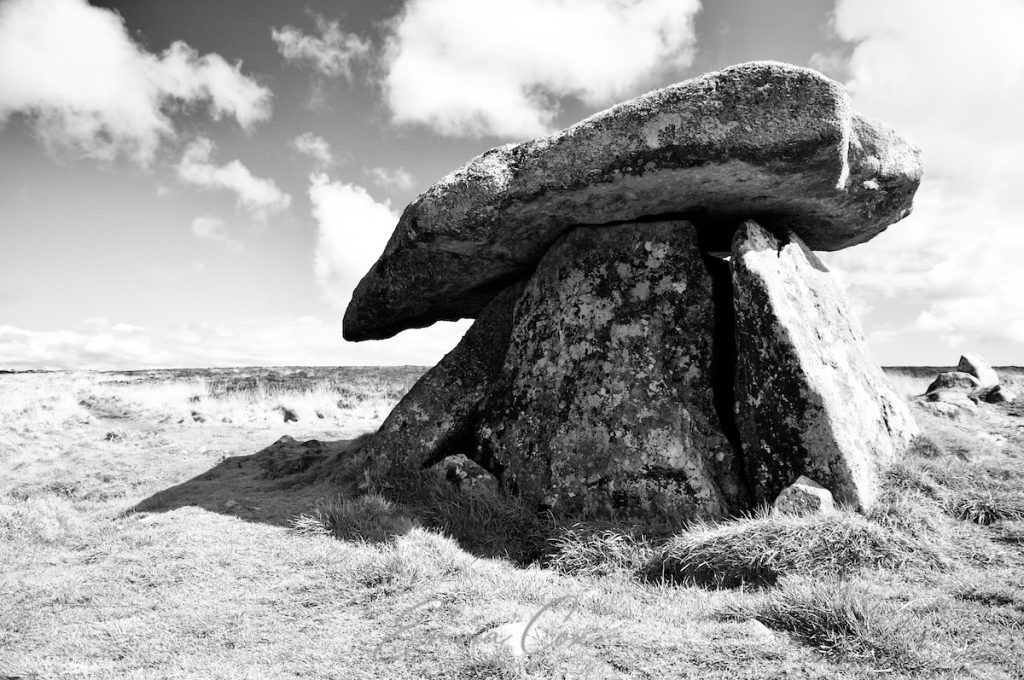 A black and white photograph of a megalithic chambered tomb consisting of four large slabs of granite, giving the structure a mushroom-like appearance.