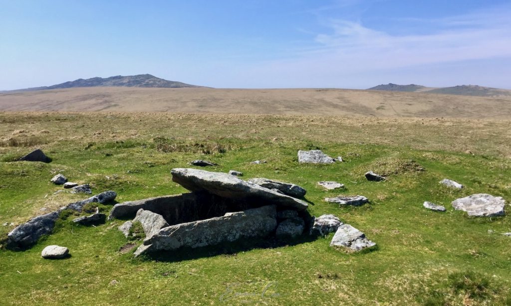 A photograph of a cist tomb, a granite box-like structure, on the high moor. In the distance are Brown Willy and Rough Tor summits on Bodmin Moor.