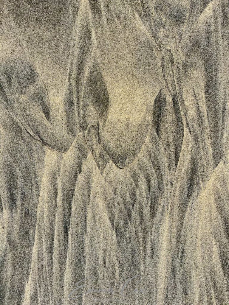 An abstract photograph of fine beach sand worked into a pattern through wave action.