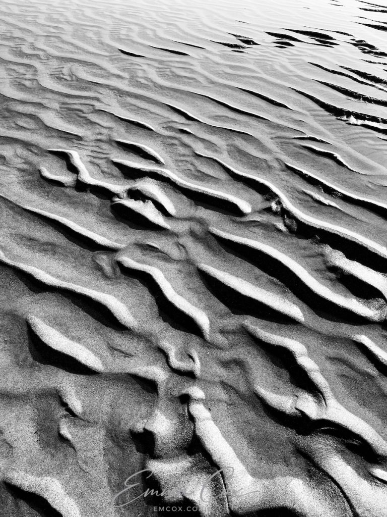 An abstract black and white photograph of beach sand worked into a rippling pattern through wave action.