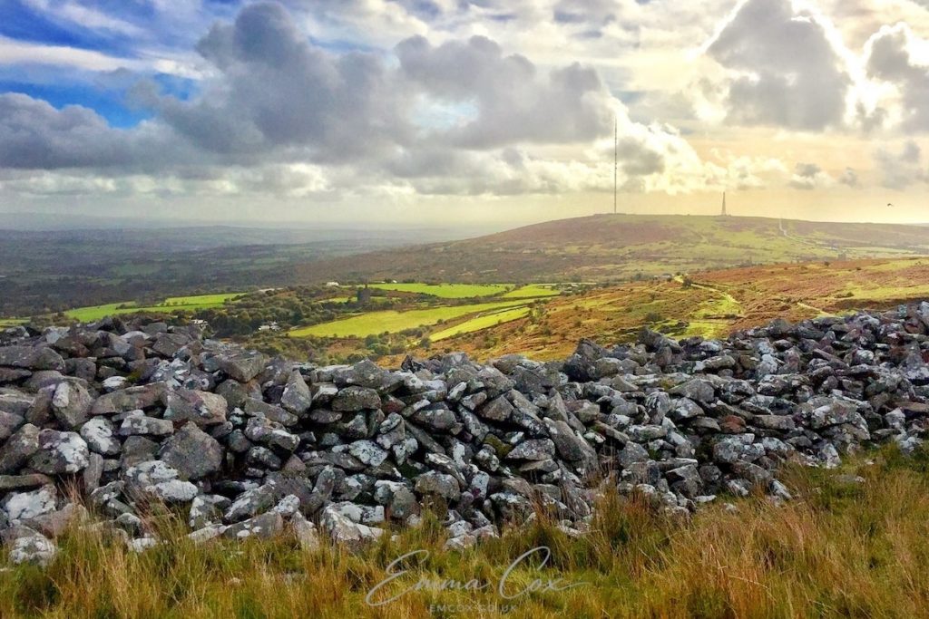 A photograph looking out over Bodmin moor. A ring of ancient perimeter stones surrounds the summit with views across the open moorland.