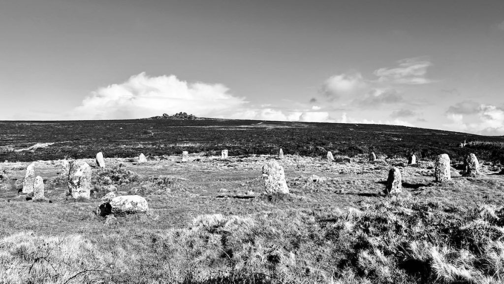 A black and white photograph of Tregeseal stone circle with a granite topped hill Carn Kenidjack in the distance.
