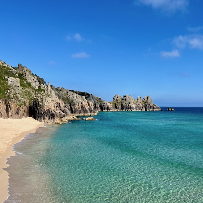 A sandy beach surrounded by granite cliffs with a distant granite headland
